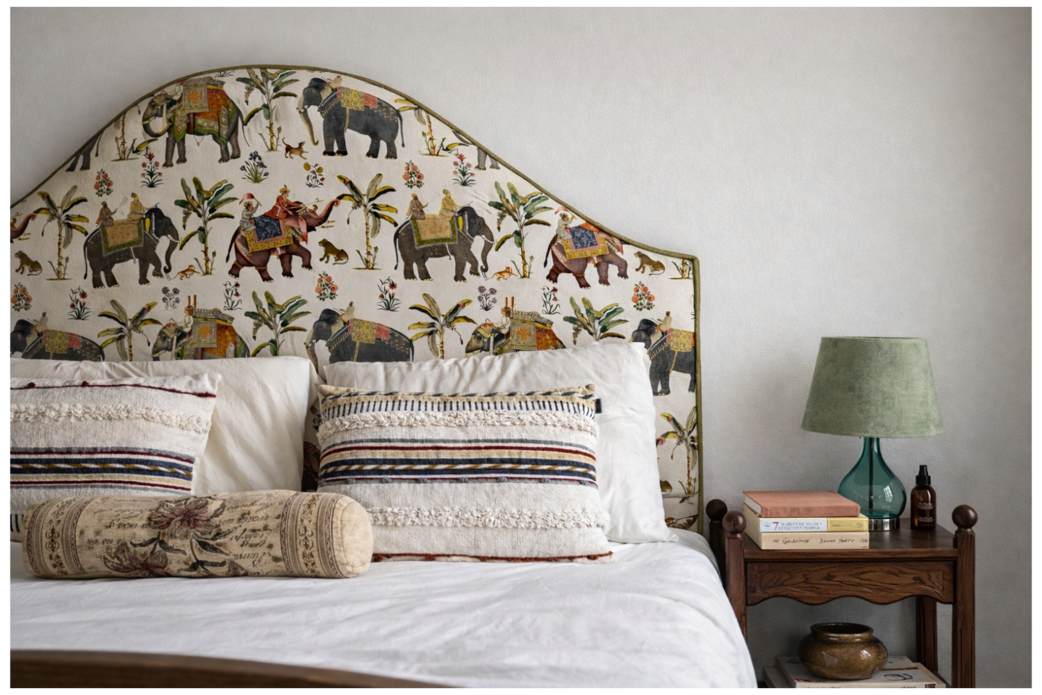 Bedroom with decorative headboard featuring animal patterns, pillows, and a nightstand with books and a lamp.