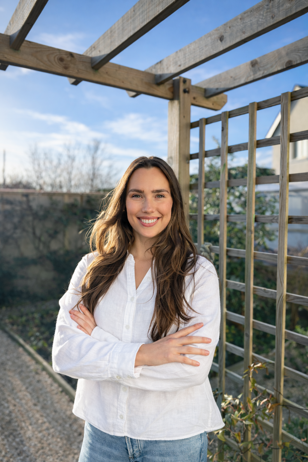 Woman in a white shirt standing under a wooden pergola with a garden background