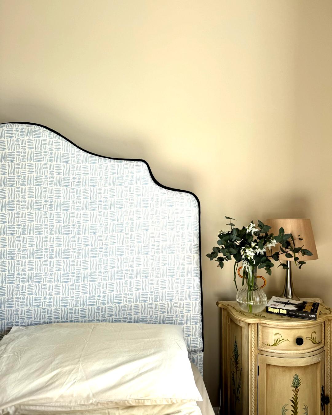 Bedroom with a textured headboard and a nightstand with a lamp and flowers.